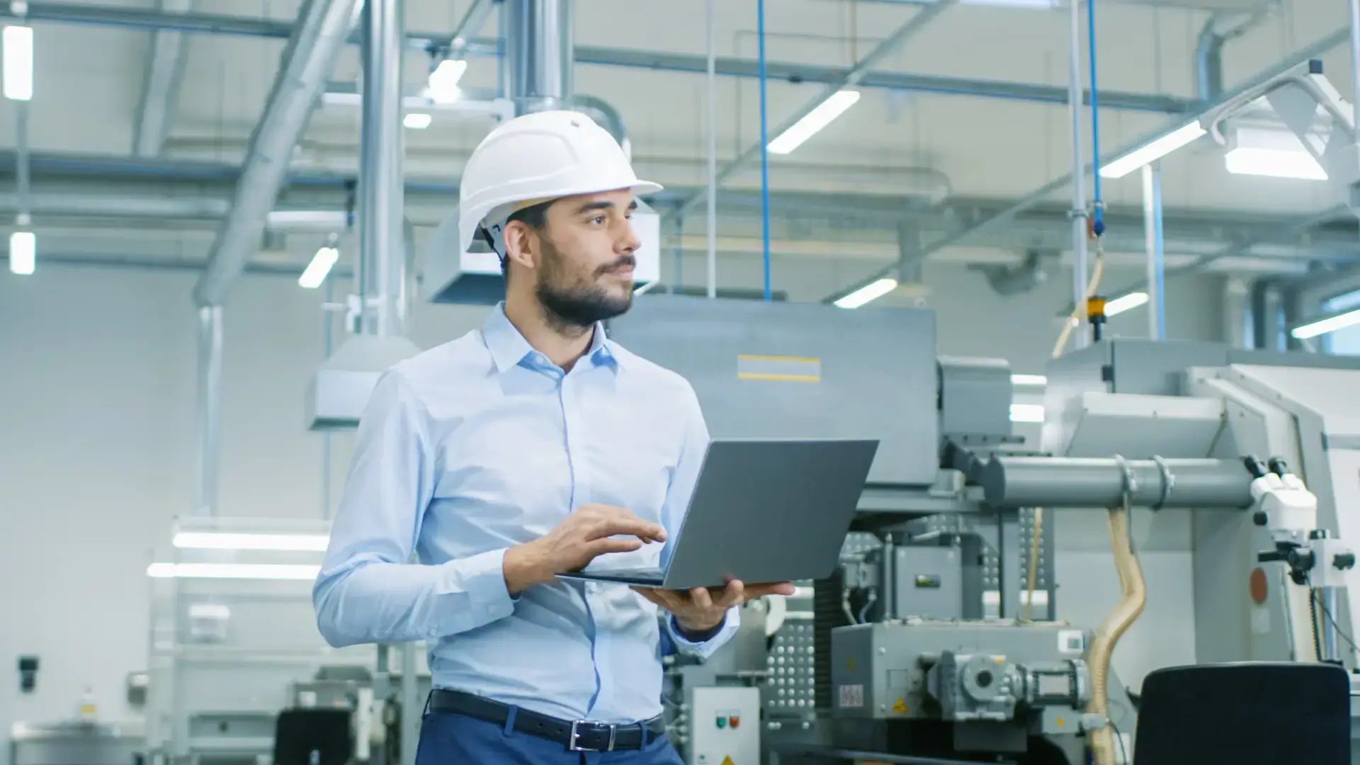 Engineer in hard hat walking through bright manufacturing facility