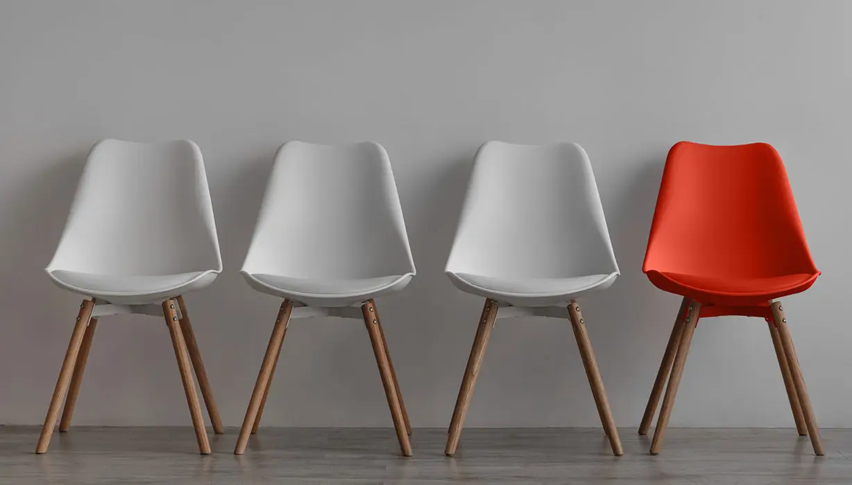 three empty white chairs and one orange chair against a wall