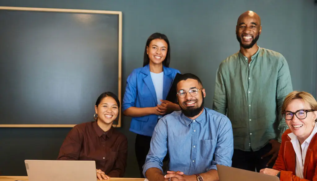 five smiling co-workers in an office at a table
