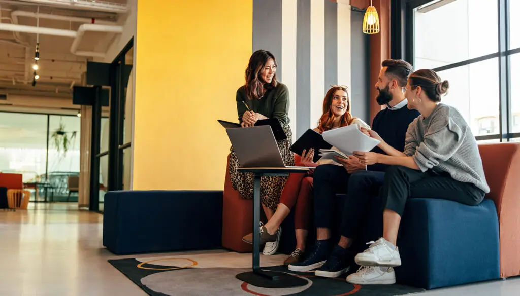 Four people sitting on a couch looking at a laptop