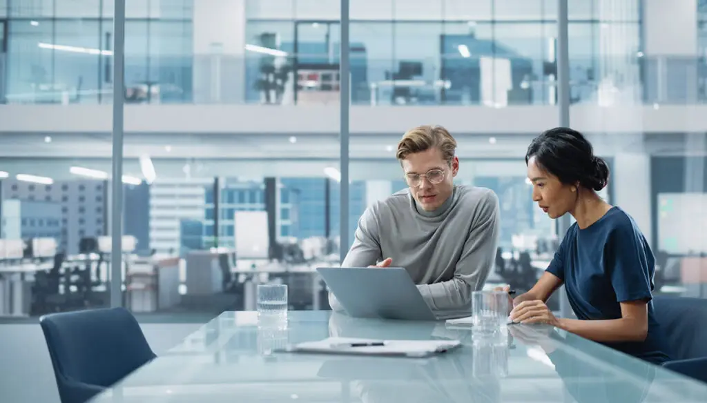 Man and woman sitting in a conference room look at a laptop