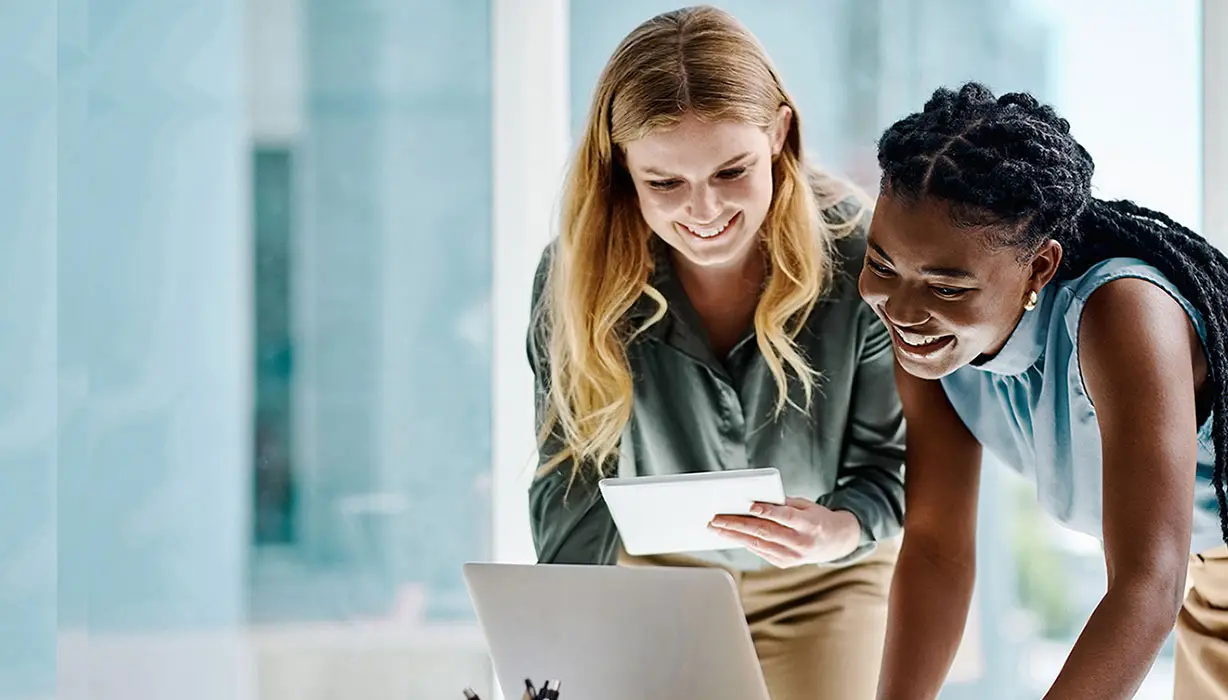 two smiling women working in an office with a laptop