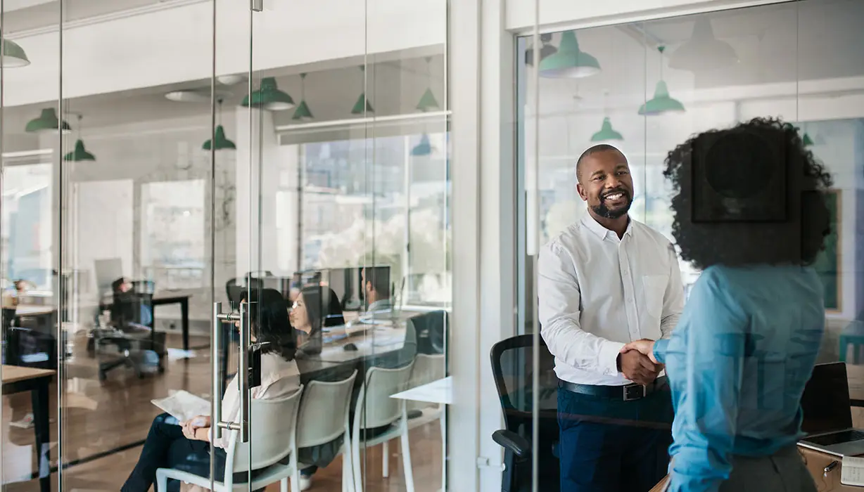 smiling man in white shirt shaking hands with woman in blue in an office