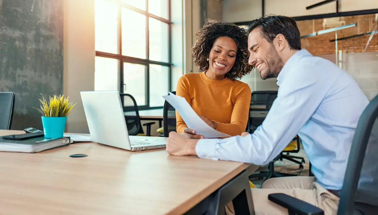 smiling man and woman in an office looking at paper