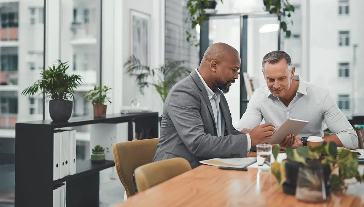 two men in an office seated at a table looking at a pad of paper